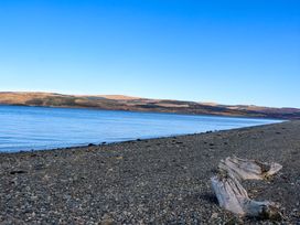 A rocky beach with driftwood by a body of water and hills in the background at Esk Lodge in Salen Isle Of Mull