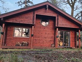 A red wooden cabin with two windows a stack of firewood and trees around Esk Lodge Salen Isle Of Mull