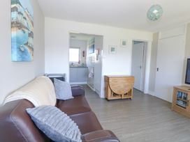 A living room with a brown sofa, gray pillows, a wooden drop-leaf table, a TV cabinet, and a view into a small kitchen at Chalet 37 in Hemsby