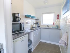 A small kitchen with grey cabinets a microwave coffee maker kettle and dishes on a shelf at Chalet 37 in Hemsby