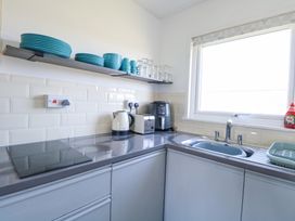 A kitchen counter with a sink toaster kettle air fryer and blue dishes on a shelf at Chalet 37 in Hemsby