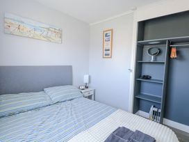 A bedroom with a bed with striped bedding bedside table with lamp and digital clock open closet shelves hangers and heater at Chalet 37 in Hemsby