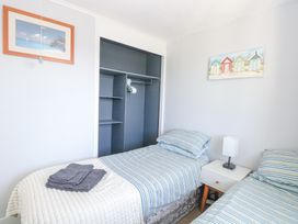 A bedroom with two single beds striped bedding a bedside table with lamp an open wardrobe and beach themed wall art at Chalet 37 in Hemsby