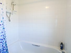 A white tiled bathroom with a bathtub shower enclosure and a shower curtain at Chalet 37 in Hemsby