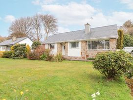 A front view of a stone and white house with a lawn and bushes at 3 Glyn Y Mor in Llanbedrog