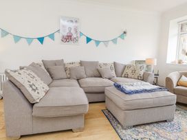 A living room with a beige sectional sofa, matching ottoman, blue bunting on wall, and an octopus picture at 3 Glyn Y Mor in Llanbedrog