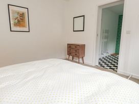 A bedroom with a bedspread with yellow dots a wooden dresser a framed picture and an open door to a bathroom with black and white checkered flooring at 3 Glyn Y Mor in Llanbedrog