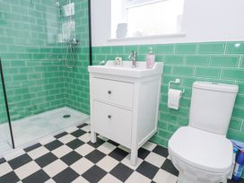 A bathroom with a shower, sink cabinet, toilet, green tiled walls, and black and white checkered floor at 3 Glyn Y Mor in Llanbedrog