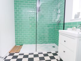 A bathroom with a walk-in shower with green tiled walls a white sink cabinet and a checkered floor at 3 Glyn Y Mor in Llanbedrog