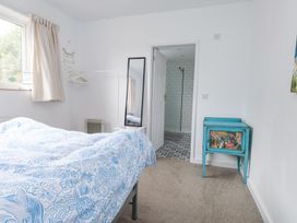 A bedroom with a bed covered in a blue and white patterned duvet a standing mirror a white clothes rack with hangers a small turquoise cabinet and a door leading to a tiled bathroom at 3 Glyn Y Mor in Llanbedrog