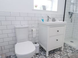 A bathroom with a toilet, a sink with a cabinet, a window, and a shower area at 3 Glyn Y Mor in Llanbedrog
