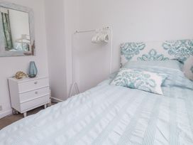 A bedroom with a bed with patterned headboard and pillows a white chest of drawers and a full-length mirror at 3 Glyn Y Mor in Llanbedrog