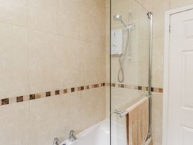 A bathroom with a bathtub shower with glass screen beige tiled walls and a towel on the rail at 3 Glyn Y Mor in Llanbedrog