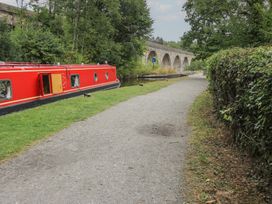 A narrowboat on a canal with a pathway and trees near a bridge at 2 Aqueduct Cottages in Chirk Bank near Chirk