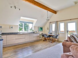 An open kitchen and dining area with wooden floor and a carpeted living space at Seascape Cottage in Beer