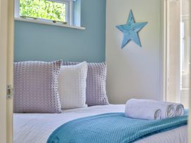 A bed with rolled white towels and pillows with a blue star wall decor at Seascape Cottage in Beer