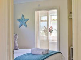 A bedroom with a bed and rolled towels looking into a bathroom with a sink and windows at Seascape Cottage in Beer