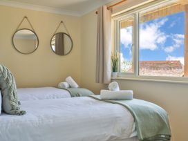 A bedroom with two single beds with white linens green throws and rolled towels by a window with two hanging round mirrors on the wall at Seascape Cottage in Beer