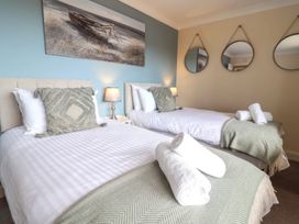 A bedroom with two single beds white linens green throw blankets pillows bedside lamps and round mirrors on the wall at Seascape Cottage in Beer