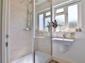 A bathroom with a walk-in shower and a wall-mounted sink under a frosted window at Seascape Cottage in Beer