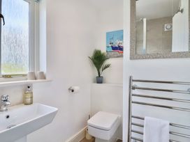 A bathroom with a sink soap dispenser window toilet towel rack and a plant on a shelf at Seascape Cottage in Beer