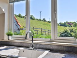 A kitchen sink with a chrome faucet and two small potted plants on the windowsill overlooking a green hillside at Seascape Cottage in Beer