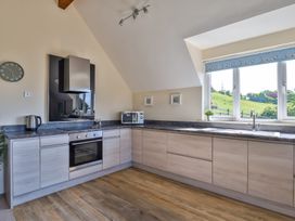 A kitchen with light wood cabinets a stove microwave kettle and a window with a view at Seascape Cottage in Beer