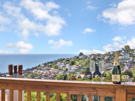A wooden balcony railing with a bottle of champagne and two empty glasses overlooking a coastal hillside village at Seascape Cottage in Beer