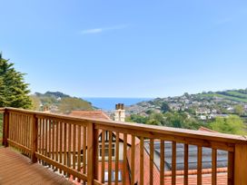 A wooden balcony railing overlooking rooftops trees hills and sea at Seascape Cottage in Beer