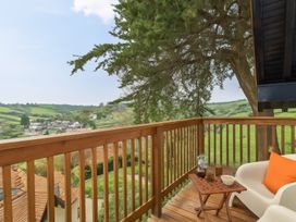 A wooden balcony with a small table and white chair overlooking green hills and houses at Seascape Cottage in Beer