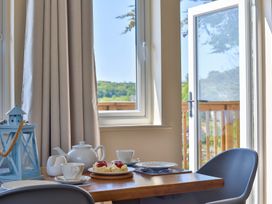 A dining table with teapot cups plates and scones near a window and open door at Seascape Cottage in Beer