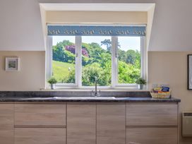 A kitchen sink under a window with a blue blind with birds and plants on the sill at Seascape Cottage in Beer