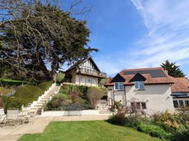 A garden with grass a patio and two houses with stairs and solar panels at Seascape Cottage in Beer
