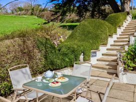 An outdoor patio with a table set for tea and a staircase with hedges at Seascape Cottage in Beer