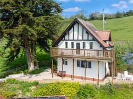 A two-story house with a wooden balcony and outdoor seating surrounded by greenery at Seascape Cottage in Beer