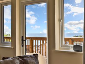 A room with windows and a glass door opening to a wooden balcony with a radio on the windowsill at Seascape Cottage in Beer