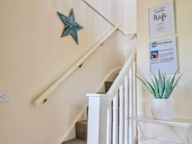 A staircase with a white railing a blue star wall decoration a plant in a white pot and framed wall signs at Seascape Cottage in Beer