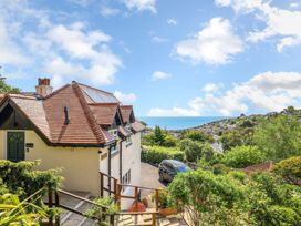 A house with a red tiled roof and solar panels surrounded by greenery with a black car parked and a sea view in Beer