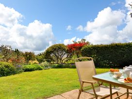 A garden with a lawn and shrubs and a table with chairs and tea set at Beer View Cottage in Beer