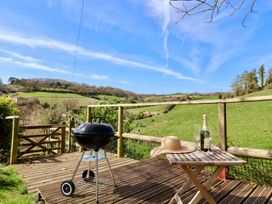 A wooden deck with a barbecue grill a small table with a sunhat champagne bottle and glasses overlooking green fields at Beer View Cottage in Beer