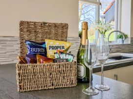 A kitchen counter with a wicker basket of snacks a bottle of champagne and two empty glasses at Beer View Cottage in Beer