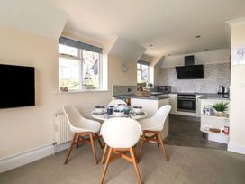 A kitchen and dining area with a round table set for four and a television on the wall at Beer View Cottage in Beer