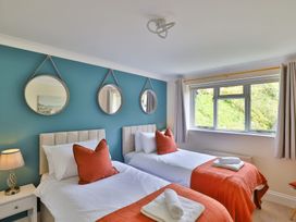 A bedroom with two single beds with orange throws and pillows and three round mirrors on a blue wall at Beer View Cottage in Beer