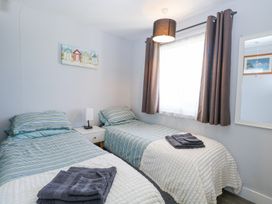 A bedroom with two single beds with striped bedding a nightstand lamp a window with brown curtains and a wall mirror at Chalet 38 in Hemsby