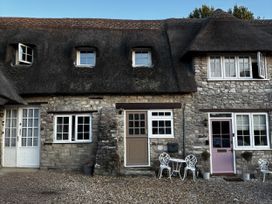 An outdoor view of a cottage with a thatched roof and stone wall at Bracken Cottage in 