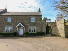 A stone cottage with white windows and door beside an arched stone gate at Pagecroft Cottage in Haydon Bridge