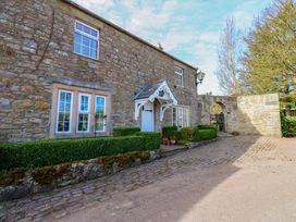 Exterior stone wall of a house with windows a white door with a small porch cobblestone pathway and trimmed hedges at Pagecroft Cottage in Haydon Bridge