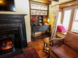 A room with a fireplace wooden cabinet dining plates vase with flowers upholstered chair and window seat at Pagecroft Cottage in Haydon Bridge