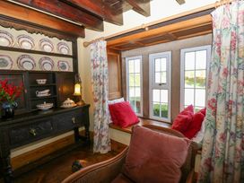 A room with a dark wooden sideboard displaying plates a window seat with red cushions and floral curtains at Pagecroft Cottage in Haydon Bridge