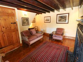 A sitting room with wooden beams a wooden door framed pictures a red patterned rug and upholstered chairs at Pagecroft Cottage in Haydon Bridge